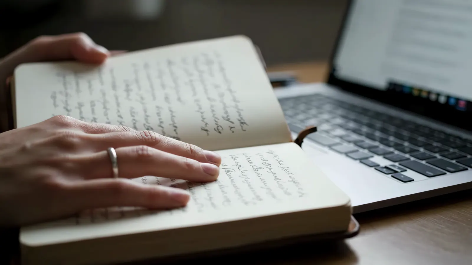 A handwritten notebook open beside a laptop.