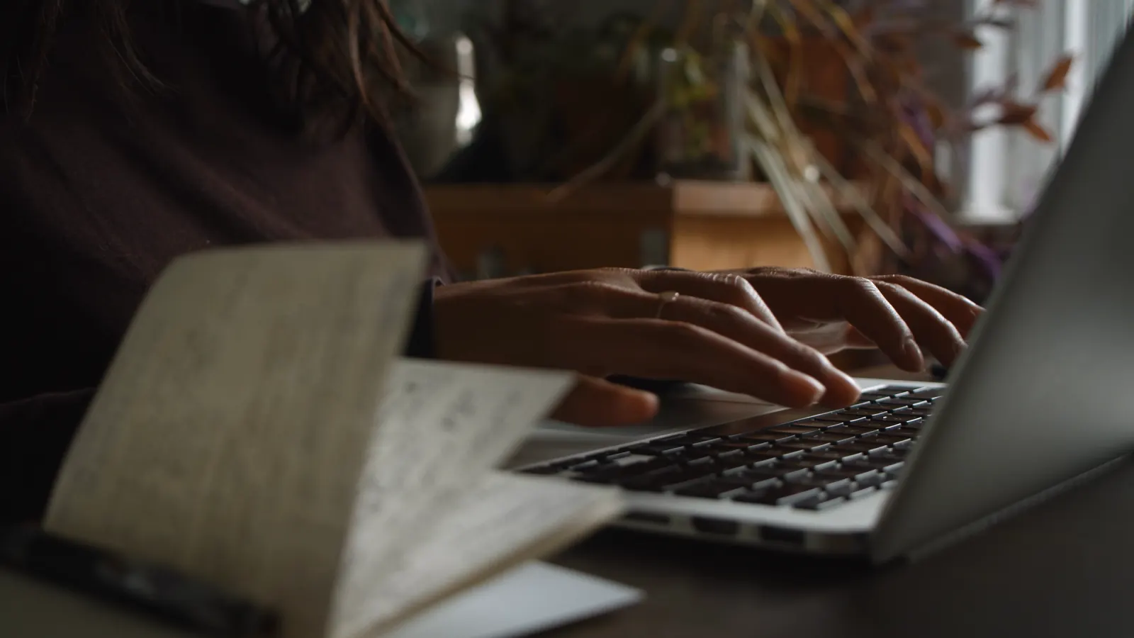 A desk in low light, a notebook open beside a screen.
